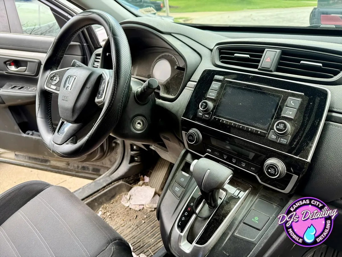 dusty car dashboard and console with debris scattered on the floor mats and around the driver seat area